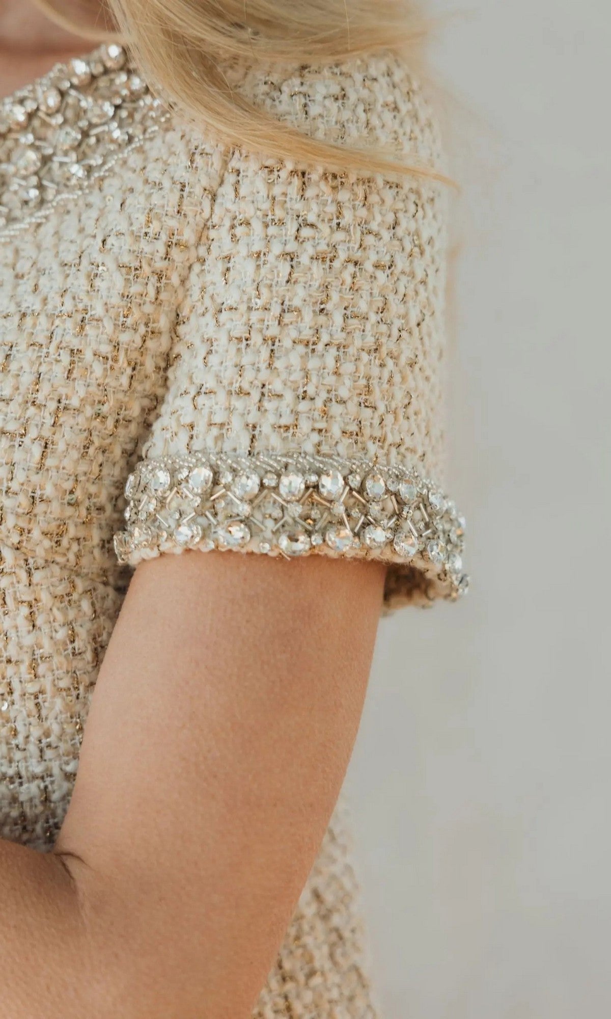 Close-up of a person wearing the Mac Duggal 37075 short semi-formal dress in beige tweed, featuring short sleeves and jeweled trim on the collar and sleeves, reminiscent of a classic boucle mini dress adorned with delicate rhinestone beading.